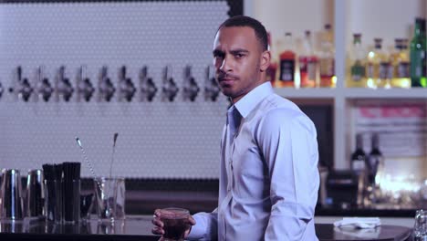 Toma-de-retrato-de-un-hombre-afroamericano-atractivo-joven-mirando-a-la-cámara-de-manera-descalzada-en-un-bar