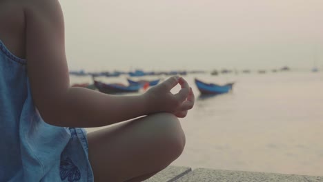 Kleine-süße-Mädchen-meditiert-in-türkischen-Pose-am-Meer