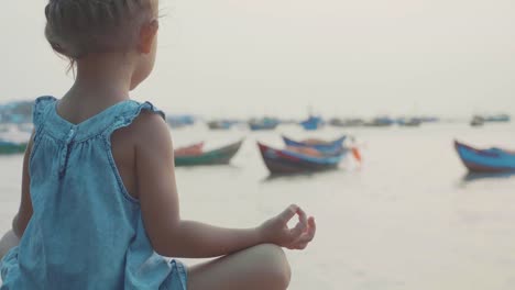 Kleine-süße-Mädchen-meditiert-in-türkischen-Pose-am-Meer