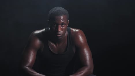 Zooming-shot-of-a-muscular-black-man-resting-in-between-workouts-on-a-foggy-dark-background