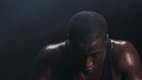 Zooming-shot-of-a-muscular-black-man-wiping-the-sweat-off-his-forehead-on-a-foggy-dark-background