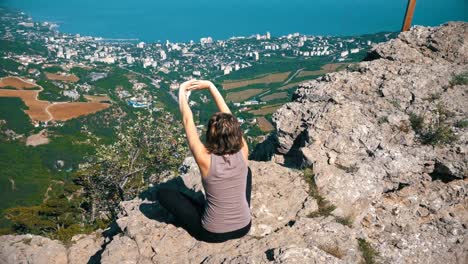 Sitting-woman-in-lotus-position-practicing-yoga-moves-or-meditates-and-Raises-her-arms-up-in-mountains