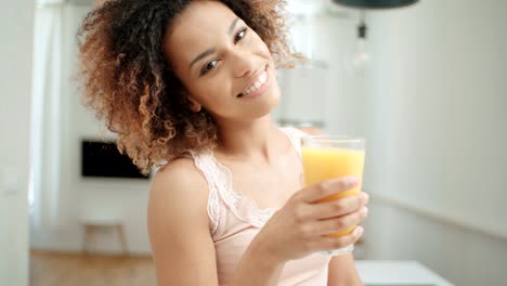 Happy-mixed-race-woman-holding-orange-juice-and-looking-to-camera.