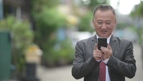 Mature-Japanese-businessman-using-phone-in-the-streets-outdoors