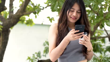 Asiatische-Frauen-Telefon-spielen-und-trinken-heißen-Kaffee-in-Coffee-Shop.