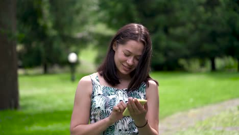 Happy-looking-asian-woman-walks-in-the-park-and-chatting-in-social-networks.