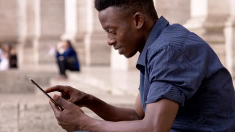 Sonriente-americana-africana-joven-usando-tableta-al-aire-libre