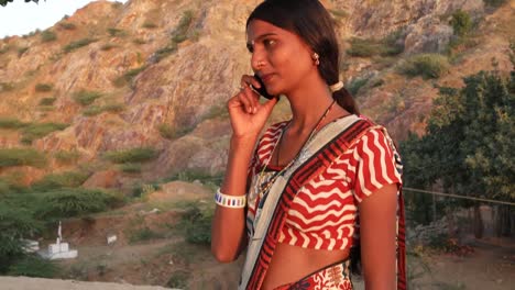 Handheld-shot-of-young-woman-talks-calls-mobile-phone-communication-device-connectivity-signal-wireless-smiles-happy-at-sunset-on-a-hill-outdoor-nature-hot-summer-day-magic-hour-beautiful-serene-love