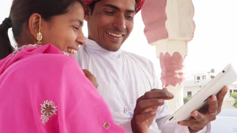 Traditional-Indian-bride-with-pink-sari-multi-coloured-bangles-on-a-pad-her-husband-in-Rajasthan,-India