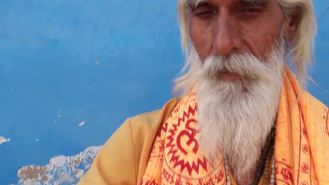 Dolly-in-to-Sadhu,-Indian-saint,-sitting-outside-a-temple-in-meditation-against-a-blue-wall