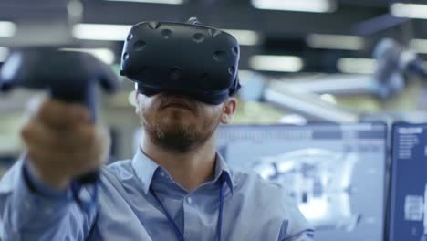 Portrait-Shot-of-the-Industrial-Engineer-Wearing-Virtual-Reality-Headset-and-Using-Controllers,-ready-to-Work.-In-the-Background-Manufacturing-Plant-and-Monitors.