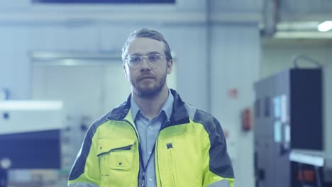 Industrial-Engineer-Wearing-Protective-Clothing-Puts-on-Hard-Hat-and-Walks-Through-Modern-Manufacturing-Facility-with-Automatic-Machinery-Working-in-Background.