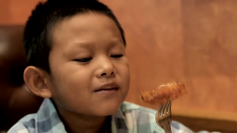 Cute-asian-boy-are-happy-eating-roasted-chicken-leg-in-restaurant.-Video-4k-Slow-motion