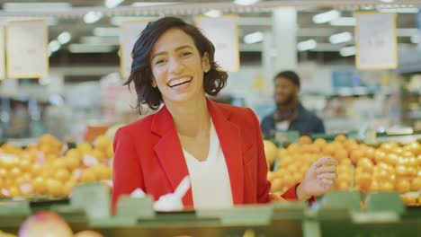 Im-Supermarkt:-Porträt-von-den-schönen-Lächeln-Frau-Wahl-Produkte-In-the-frisch-produzieren-Gang-und-legt-sie-in-den-Warenkorb.-Im-Hintergrund-bunten-Obst-und-Bio-Gemüse.-Slow-Motion.