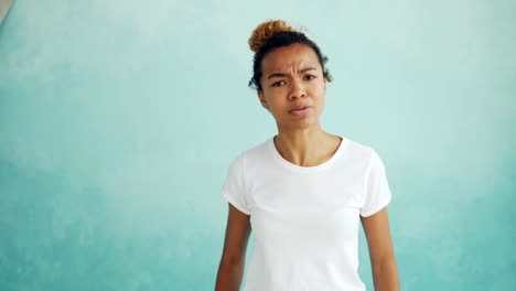 Portrait-of-angry-mixed-race-woman-talking-and-gesturing-expressing-negative-emotions-standing-against-light-blue-background.-Feelings-and-people-concept.