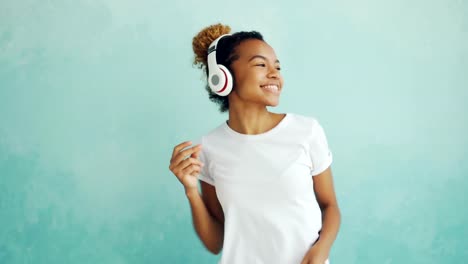 Retrato-de-mujer-afroamericana-feliz-escuchando-música-con-auriculares-inalámbricos-y-bailar-disfrutando-de-la-melodía.-Tecnología-moderna,-el-concepto-de-gente-y-diversión.