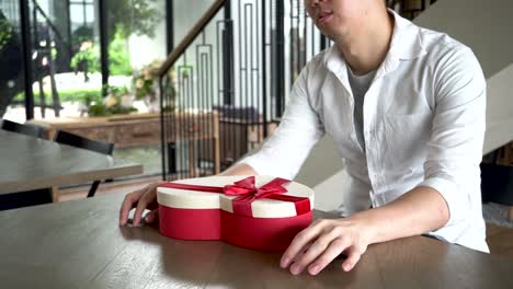 Young-man-impatiently-sitting-in-cafe-restaurant-and-holding-a-present-gift-giving-to-someone-special-for-special-occasion