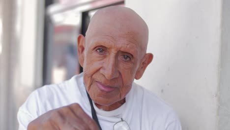 An-old-hispanic-man-stares-into-the-camera-while-sitting-on-the-street-in-Mexico