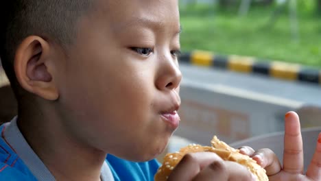 Cerca-niño-asiáticos-comer-hamburguesa,-lindo-muchacho-feliz-con-hamburguesa-en-el-restaurante.-Video-Slow-motion