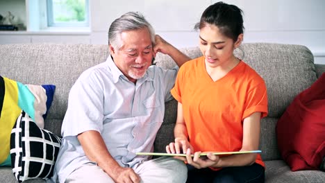 Tochter-Lesebuch-zu-ihrem-alten-Mann-Vater-im-Wohnzimmer.-Asiatische-senior-Mann-mit-weißem-Bart-und-Asiatin.-Familie-Senior-Lifestyle-Konzept.