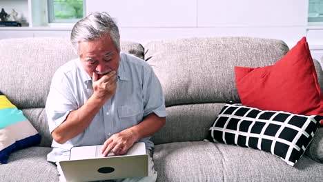 Old-man-trying-to-use-computer-in-living-room.-Asian-man-with-white-beard-using-laptop,-upset-mood.-Senior-lifestyle-concept.