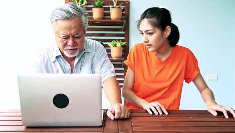 Tochter-Unterricht-ihres-Vaters-Computerkenntnisse-in-Balkon.-Asiatischer-Mann-mit-weißem-Bart-und-junge-Frau-sitzt-im-Balkon-mit-Laptop.-Familie-Senior-Lifestyle-Konzept.