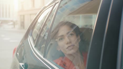 Schöne-glückliche-Frau-reitet-auf-dem-Rücken-Beifahrersitz-eines-Autos,-schaut-aus-dem-Fenster-verträumt.-Blick-auf-die-große-Stadt-spiegelt-sich-im-Fenster.-Kamera-Auto-außen-bewegen.