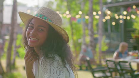 Retrato-de-hermosa-niña-negra-en-un-sombrero-sonriendo-encantadoramente,-tocar-su-pelo.-Chica-atractiva-en-un-día-de-verano-se-relaja-en-el-jardín.-En-cámara-lenta.