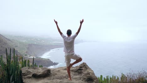 Un-hombre-de-pie-en-una-mano-en-las-montañas-de-espaldas-a-la-cámara-mirando-al-mar-y-meditar-en-las-Islas-Canarias.