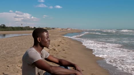 lonely-young-black-african-man-sitting-on-the-beach-contemplating-the-sea