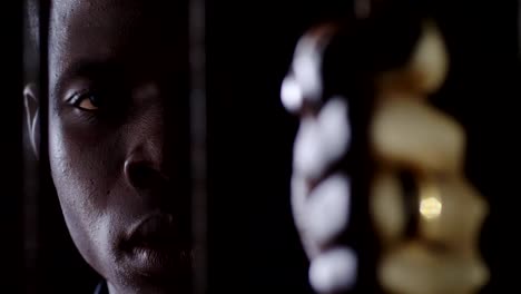 Joven-africano-preso-entre-rejas-mirando-a-cámara.-Penal,-prisión,-ley