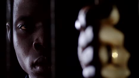 Young-african-prisoner-behind-bars-staring-at-camera.-Criminal,prison,law