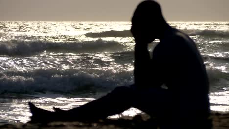 Migración,-desesperación.-Silueta-de-hombre-triste-sentado-en-la-playa