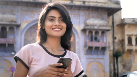 An-attractive-girl-using-smartphone-or-cellphone-is-smiling-looking-at-the-camera