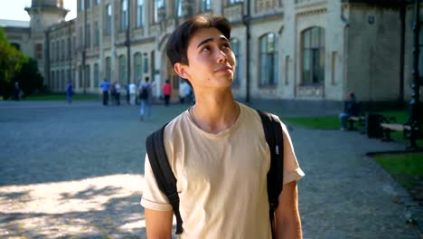 Nice-asian-male-is-looking-up-and-straight-after,-enjoying-summer-days,-being-near-great-old-buildings