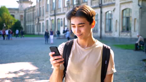 Asiatischen-gut-aussehende-Mann-ist-sein-Handy-scrollen-und-mit-einem-Blick-auf-Kamera-Kälte,-im-Freien,-urbane-Stimmung