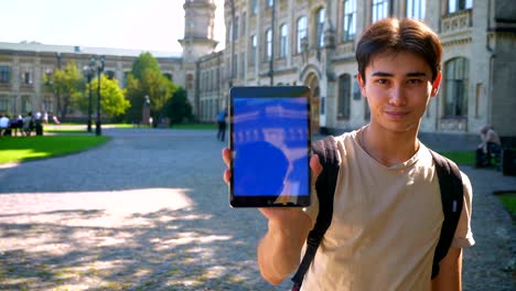 Cute-asian-man-is-standing-and-showing-blue-screen-at-camera-,-relaxed-position-and-calm-face,-ancient-architecture-behind,-sunlights