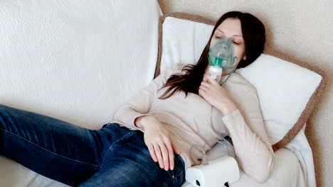 Verwenden-Sie-Vernebler-und-Inhalator-für-die-Behandlung.-Junge-Frau-Einatmen-durch-Inhalator-Maske-auf-der-Couch-liegen.-Ansicht-von-vorne.