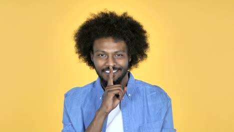 Hombre-afroamericano-gesticular-silencio,-dedo-en-los-labios,-fondo-amarillo