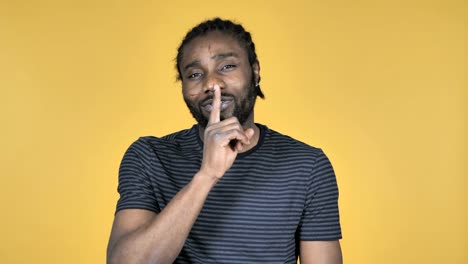 Casual-African-Man-Gesturing-Silence,-Finger-on-Lips,-Yellow-Background