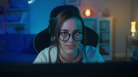 Aufgeregt-und-ziemlich-Gamer-Mädchen-in-Gläsern-ist-spielen-Online-Video-Spiel-auf-ihrem-PC.-Zimmer-und-PC-haben-bunte-warme-Led-Neonlichter.-Gemütlichen-Sie-Abend-zu-Hause.