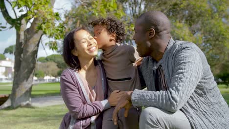 Fröhliche-multikulturelle-Eltern-umarmen-und-küssen-Sohn