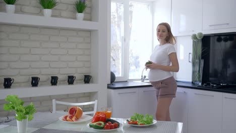 embarazo-saludable,-cuidado-a-futura-madre-beber-jugo-fresco-vitamina-y-acariciando-el-vientre-durante-el-desayuno-saludable-en-la-cocina-en-Apartamento