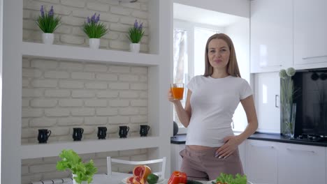 vitaminas-para-el-embarazo,-sonriendo-a-feliz-mujer-embarazada-con-Panza-grande-beber-jugo-de-frutas-durante-el-desayuno-saludable-en-la-cocina-en-Apartamento