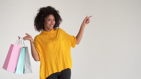 Happy-woman-holding-shopping-bags-presenting-on-studio-background-and-giving-thumbs-up-gesture