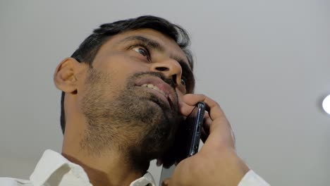 Looking-up-static-shot-of-a-man-with-stubble-talking-on-a-smart-phone-device