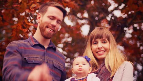 Retrato-de-una-joven-familia-bajo-un-árbol,-el-padre-intenta-sacar-el-bebé-un-mirar-la-cámara,-con-hermoso-bokeh