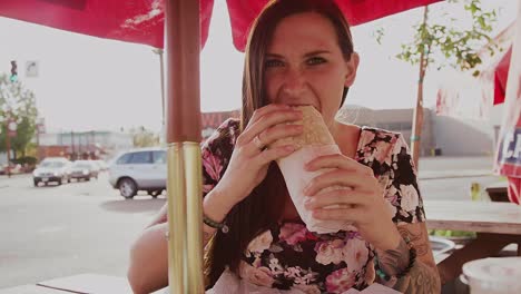 A-beautiful-girl-at-an-outdoor-table-eating-a-burrito,-slow-motion