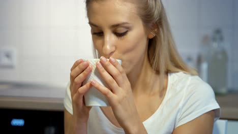 Cheerful-young-woman-holding-mug-in-the-kitchen-at-home.