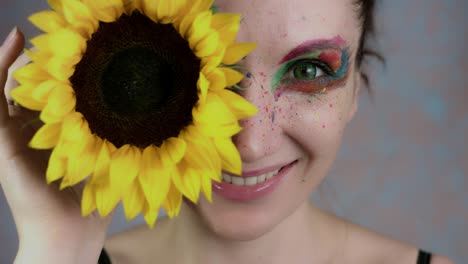 4k-Shot-of-a-Woman-with-Multicoloured-Make-up-With-Sunflower-(focus-on-eye)